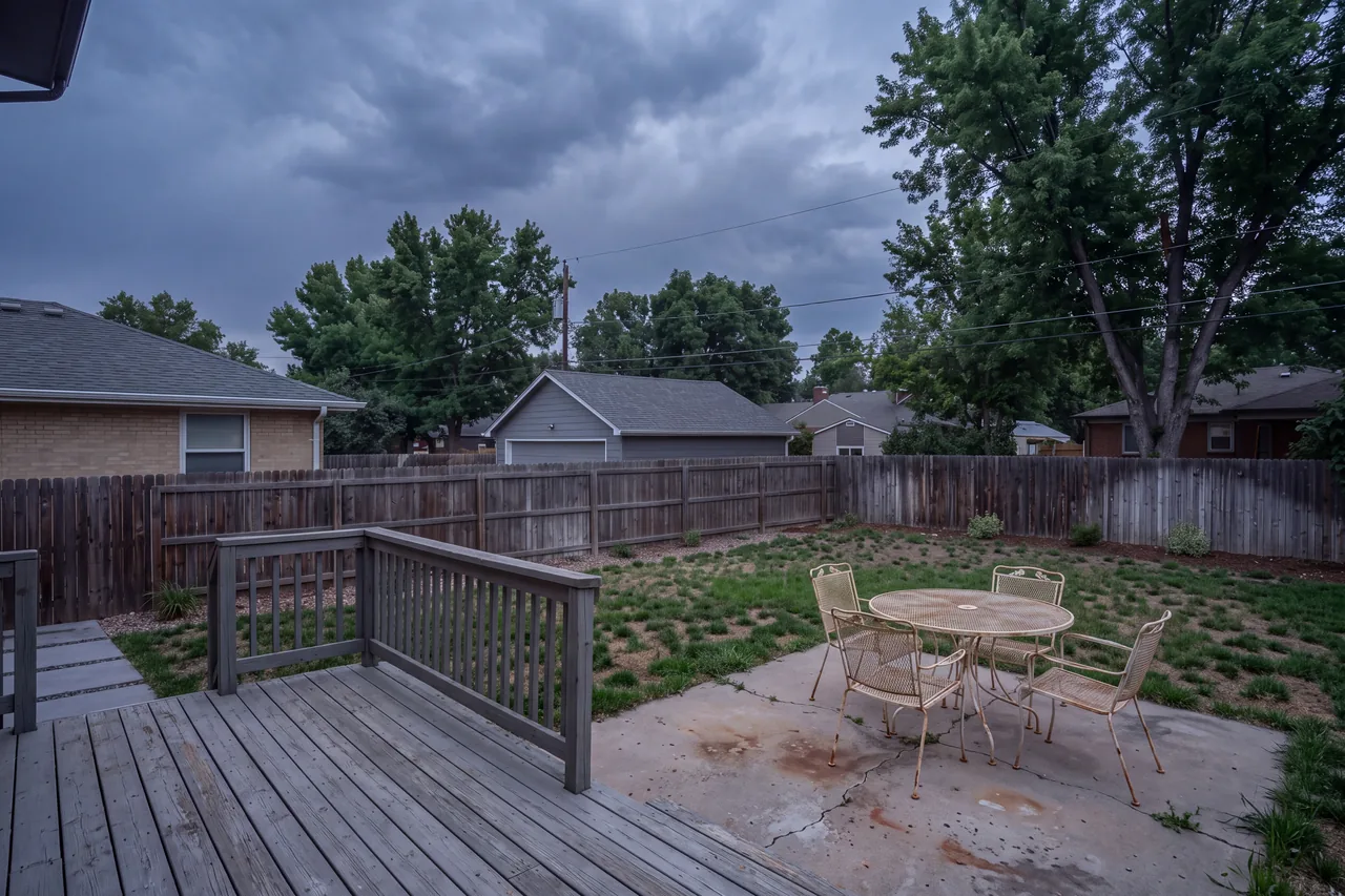 A small weathered deck and patchy lawn in a fenced backyard