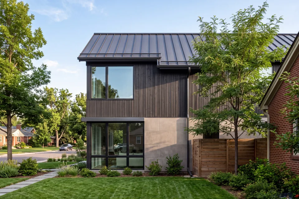 A new standing-seam metal roof, dark timber siding, limestone panels and black-framed windows on a house beside a neighboring brick house